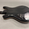 Glossy black electric guitar body with natural wood binding and rear control cavity cover on gray background