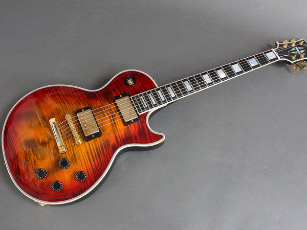 Electric guitar with sunburst flame maple top, gold hardware, and block inlays on fretboard against grey background