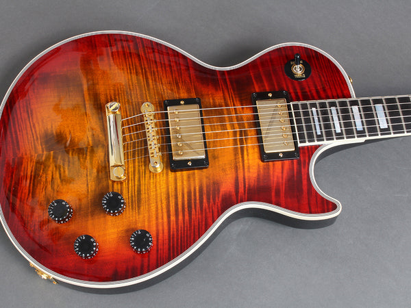 Close-up of red sunburst electric guitar with gold humbucker pickups, black control knobs, and toggle switch on grey background