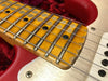 Close-up of worn maple guitar fretboard with black dot inlays, steel frets, and strings on red electric guitar body.