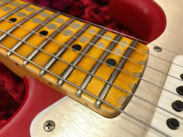Close-up of worn maple guitar fretboard with black dot inlays, steel frets, and strings on red electric guitar body.