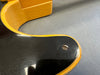 Close-up of vintage electric guitar body showing black finish with yellow binding and a metal screw on a gray surface