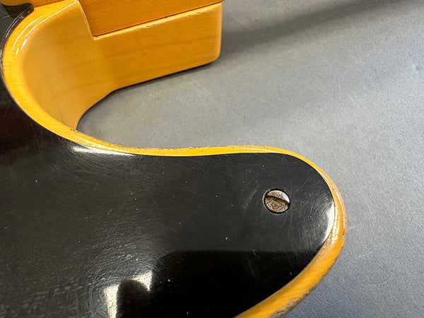 Close-up of vintage electric guitar body showing black finish with yellow binding and a metal screw on a gray surface