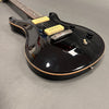 Black electric guitar with cream-colored pickups, chrome bridge, and black control knobs on gray surface