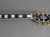 Close-up of Gibson guitar headstock and fretboard with mother of pearl inlays and gold tuning pegs on a gray background
