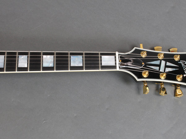 Close-up of Gibson guitar headstock and fretboard with mother of pearl inlays and gold tuning pegs on a gray background