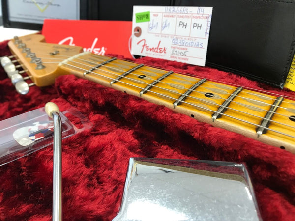 Close-up of Fender electric guitar neck and strings resting in red plush-lined hard case with Fender tag and tremolo arm visible