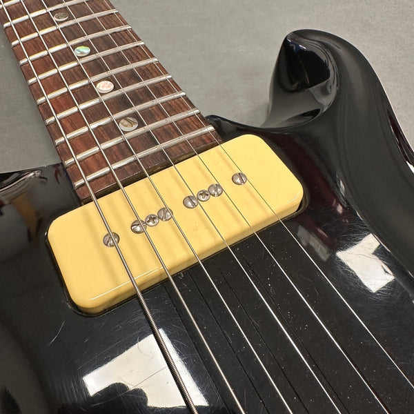 Close-up of black electric guitar with yellow P-90 single coil pickup and rosewood fretboard with pearl dot inlays