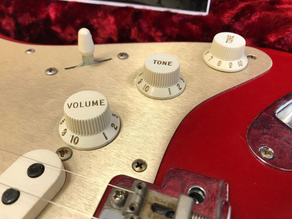 Close-up of vintage electric guitar control knobs and switch on red and cream pickguard showing volume and tone dials with strings and pickup visible
