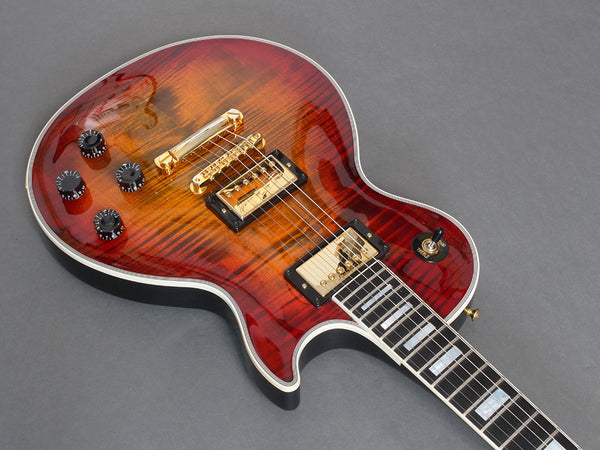Electric guitar with flame maple top in sunburst finish, gold hardware, and black control knobs on gray background