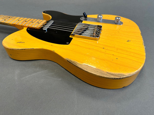 Vintage-style yellow Telecaster electric guitar with maple neck and black pickguard showing wear and natural wood finish on body edge