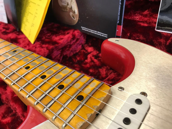 Close-up of vintage electric guitar maple neck and fretboard with metal frets and black dot inlays, cream-colored body with red binding, and single-coil pickup in red plush guitar case