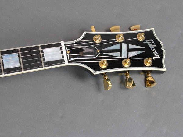 Close-up of Gibson guitar headstock with mother-of-pearl inlay and gold tuning pegs on gray background