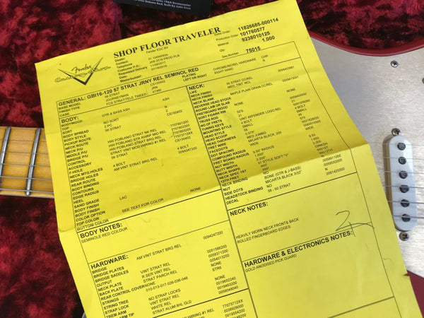 Fender Custom Shop Shop Floor Traveler yellow build sheet placed on a Seminole Red guitar body with white single-coil pickups on red plush background