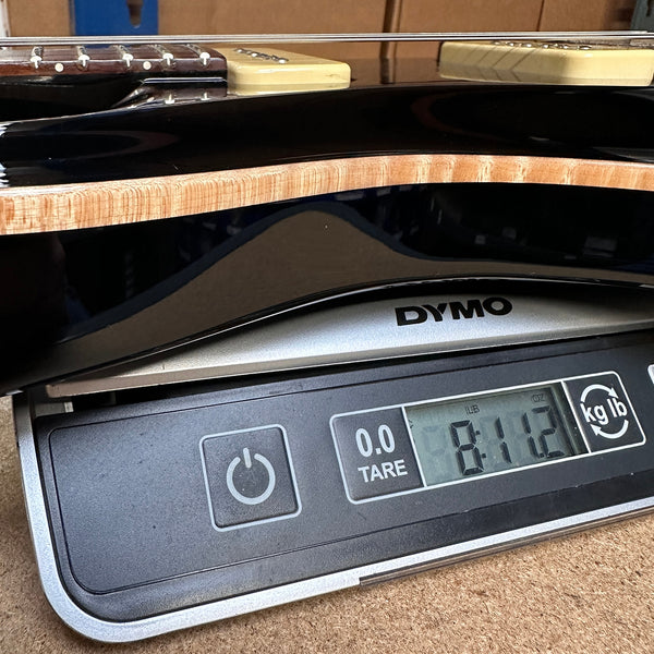 Electric guitar body placed on DYMO digital scale showing weight of 8.11 pounds at Coffee House Guitars.