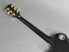 Back of black Gibson electric guitar neck showing gold tuning pegs and Gibson logo plate on a gray background
