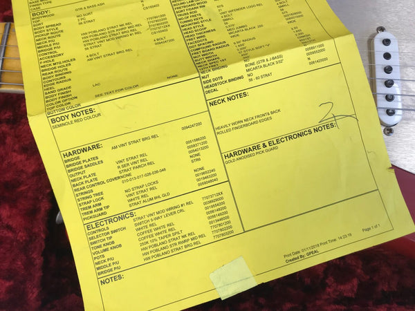 Coffee House Guitars product spec sheet on yellow paper detailing body, hardware, electronics, and neck notes for a 1956 Stratocaster guitar with Seminole Red colour and gold anodised pick guard, laid on a red guitar case with part of a white guitar pickup and strings visible.