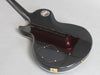 Back view of black electric guitar with glossy finish and gold hardware, showing control cavity cover and serial number plate at Coffee House Guitars