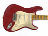 Red electric guitar with three single-coil pickups, cream pickguard, and maple fretboard with dot inlays, vintage style controls and bridge, isolated on white background.