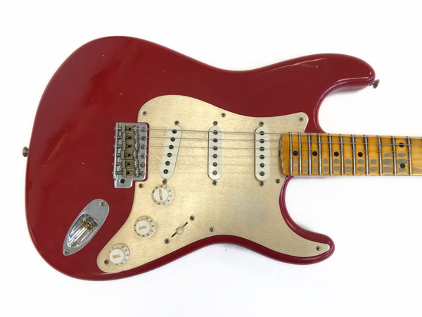 Red electric guitar with three single-coil pickups, cream pickguard, and maple fretboard with dot inlays, vintage style controls and bridge, isolated on white background.