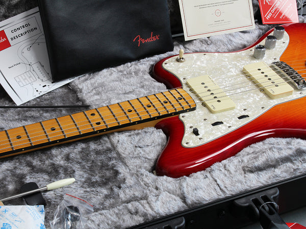 Fender electric guitar with sunburst finish and maple neck inside a plush guitar case with Fender branded accessories and documentation.