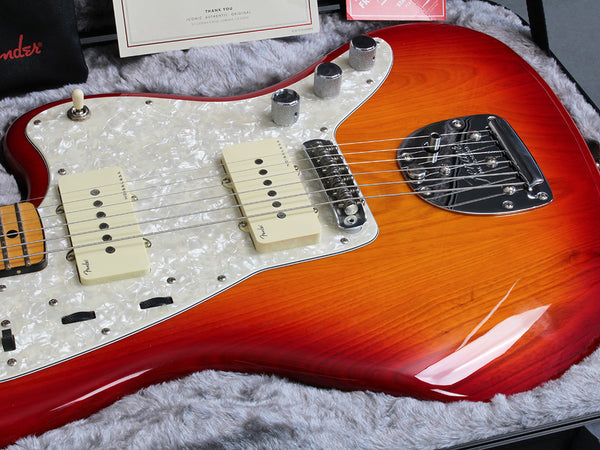 Close-up of a sunburst Fender electric guitar with pearl white pickguard, dual single-coil pickups, chrome bridge, and control knobs in a gray plush guitar case.