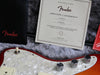 Fender certificate of authenticity next to red and white electric guitar body with chrome knobs and white toggle switch on gray fur background