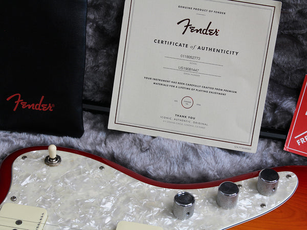 Fender certificate of authenticity next to red and white electric guitar body with chrome knobs and white toggle switch on gray fur background