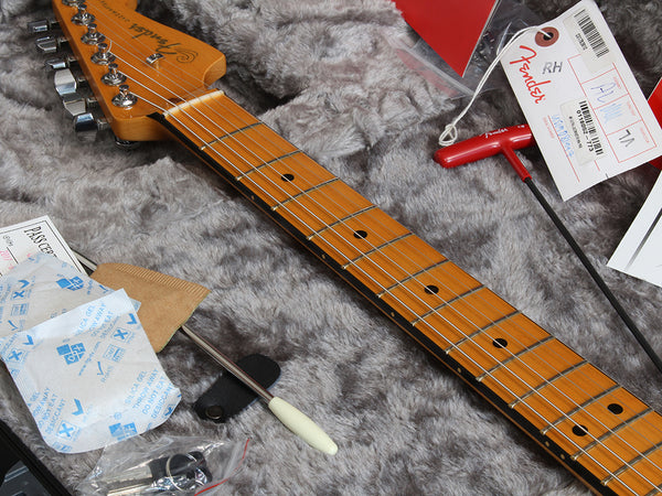Close-up of Fender electric guitar neck and headstock with maple fretboard, showing tuning pegs, included truss rod adjustment tool and accessories on gray plush guitar case lining.