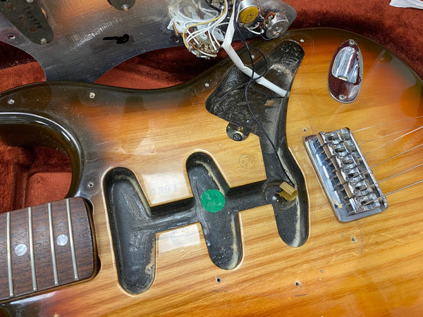 Close-up of sunburst electric guitar body showing pickup cavities, bridge, and internal wiring with pickguard removed, revealing guitar electronics cavity and wood grain detail