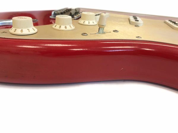 Close-up view of red electric guitar body with cream control knobs for tone and volume and three single-coil pickups on white pickguard