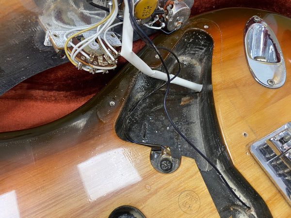 Close-up of vintage electric guitar body showing internal wiring, control pot, and pickup cavity with aged wood finish and metal output jack plate.