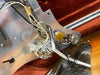 Close-up of vintage electric guitar wiring and potentiometers inside a sunburst guitar body with a metallic control plate and orange velvet case lining.