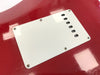 Close-up of white backplate covering guitar tremolo cavity on red electric guitar body with visible screws