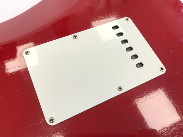 Close-up of white backplate covering guitar tremolo cavity on red electric guitar body with visible screws