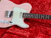 Close-up of vintage pink electric guitar body with white pickguard and rosewood fretboard on red plush fabric background