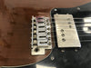 Close-up of electric guitar bridge, strings, and humbucker pickup on brown and black guitar body with visible screws and saddles