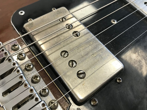 Close-up of vintage Fender guitar pickup and bridge with metal screws and six strings on a black and brown electric guitar body