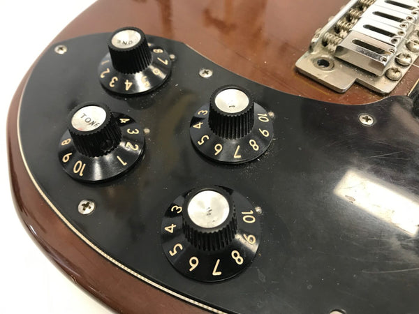 Close-up of black control knobs and tone dial on brown electric guitar with black pickguard and metal bridge screws visible