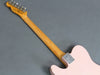 Back view of pink Fender electric guitar with maple neck and chrome neck plate on gray background