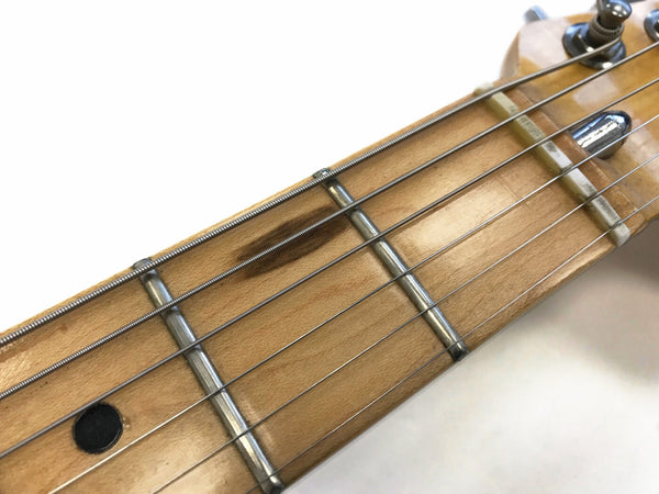 Close-up image of a maple guitar neck fretboard showing metal frets, steel strings, and a black dot position marker.