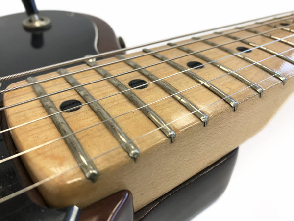 Close-up of electric guitar maple fretboard with metal frets and black dot inlays, showing six steel strings and part of black guitar body on white background