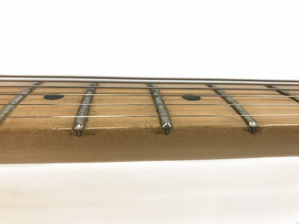 Close-up of maple guitar neck fretboard with metal frets and black dot inlays, six steel guitar strings against white background