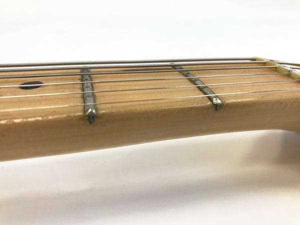 Close-up of guitar neck and frets with steel strings on light wood fretboard, detailed view of string winding and fret markers against white background