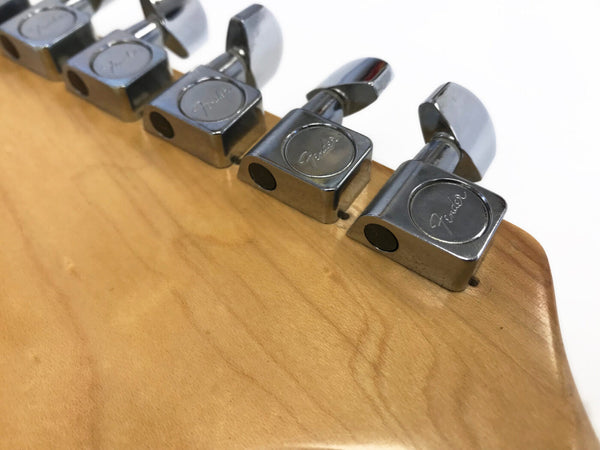 Close-up of chrome Fender tuning pegs on natural wood guitar headstock against white background