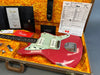 Fender electric guitar in red finish with white pickguard and vintage-style pickups displayed in open orange plush-lined hard case, accompanied by Fender certificate of authenticity and shop floor travel documents.