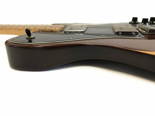 Close-up side view of dark brown electric guitar body with black pickguard, metal pickups, toggle switch, and control knobs on white background