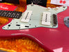 Close-up of vintage red Fender electric guitar body with white pickups and knobs, showing worn finish and age marks in orange plush-lined guitar case with Fender booklet and price tags visible.