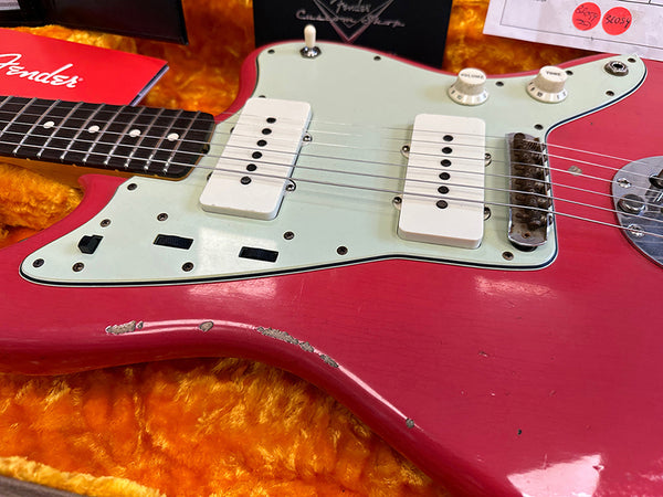 Close-up of vintage red Fender electric guitar body with white pickups and knobs, showing worn finish and age marks in orange plush-lined guitar case with Fender booklet and price tags visible.