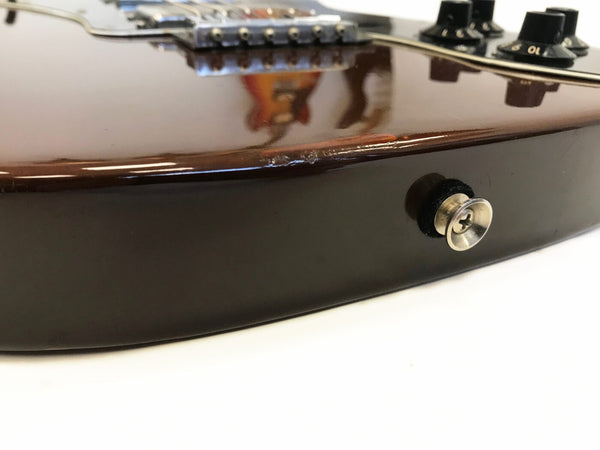 Close-up of a dark glossy electric guitar body showing a strap button and a small area of damage on the side edge with guitar bridge and control knobs in soft focus